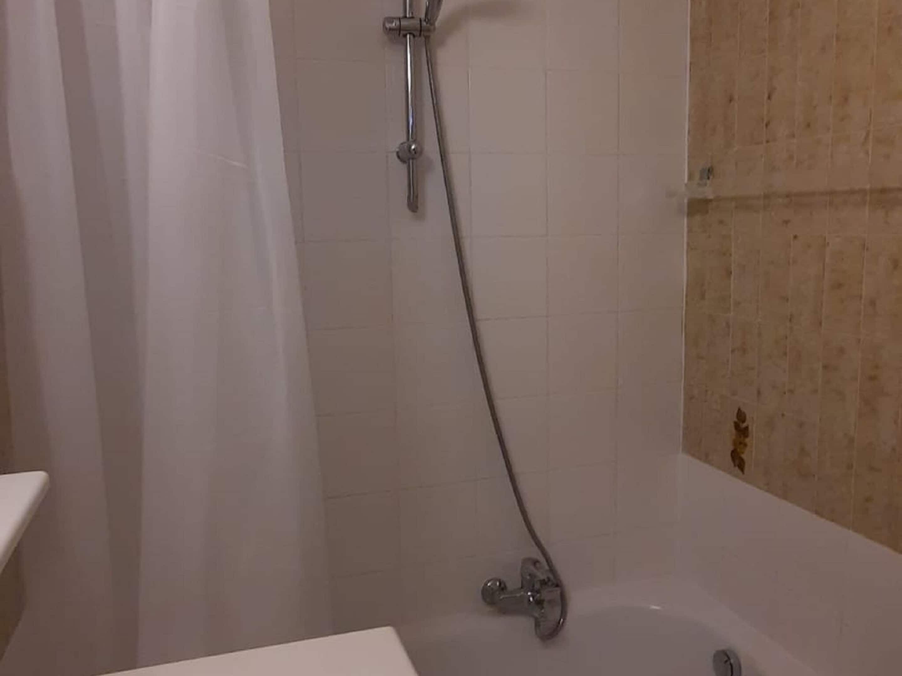 Een badkamer met een bad, een douchekop en een gordijn.