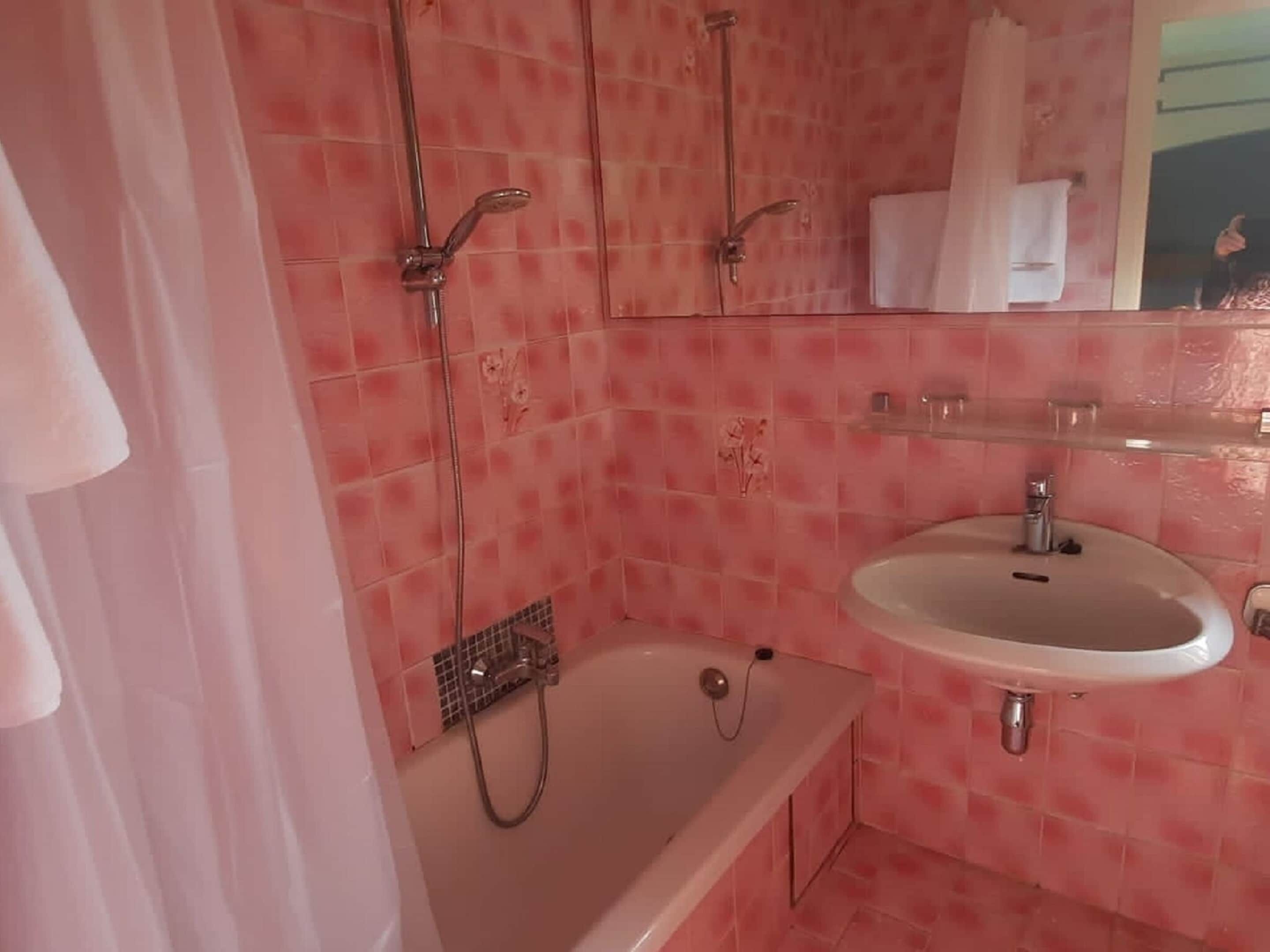 Casa de banho com azulejos cor-de-rosa, banheira, lavatório e espelho.