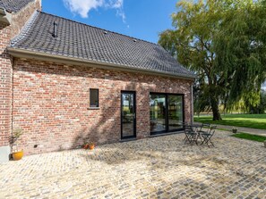 A brick building with a tiled roof, a glass door, and a paved patio with outdoor furniture.