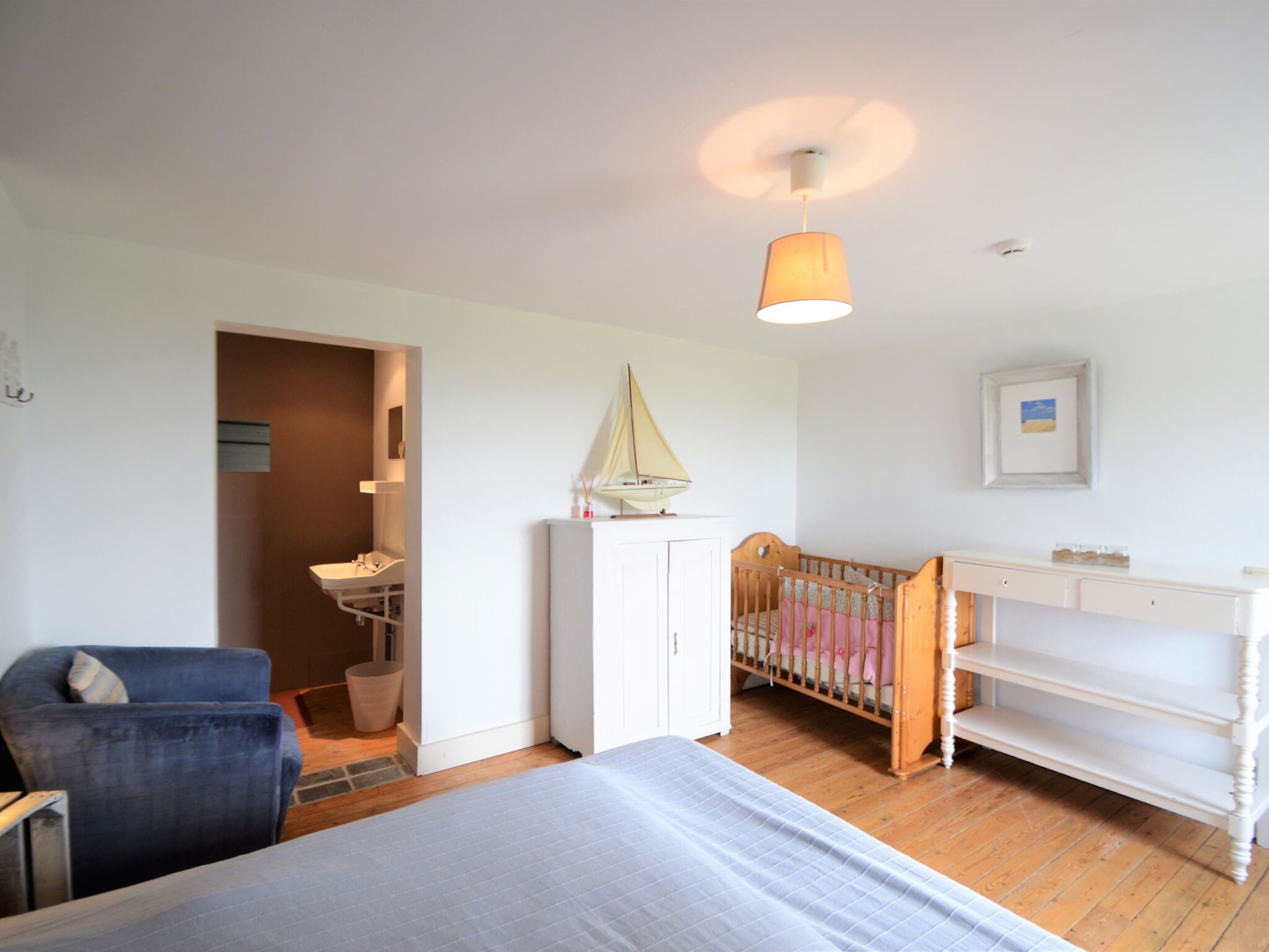 Ein Schlafzimmer mit einem Bett, einem Schreibtisch, einem Stuhl, einem Babybett und einer Pendelleuchte.