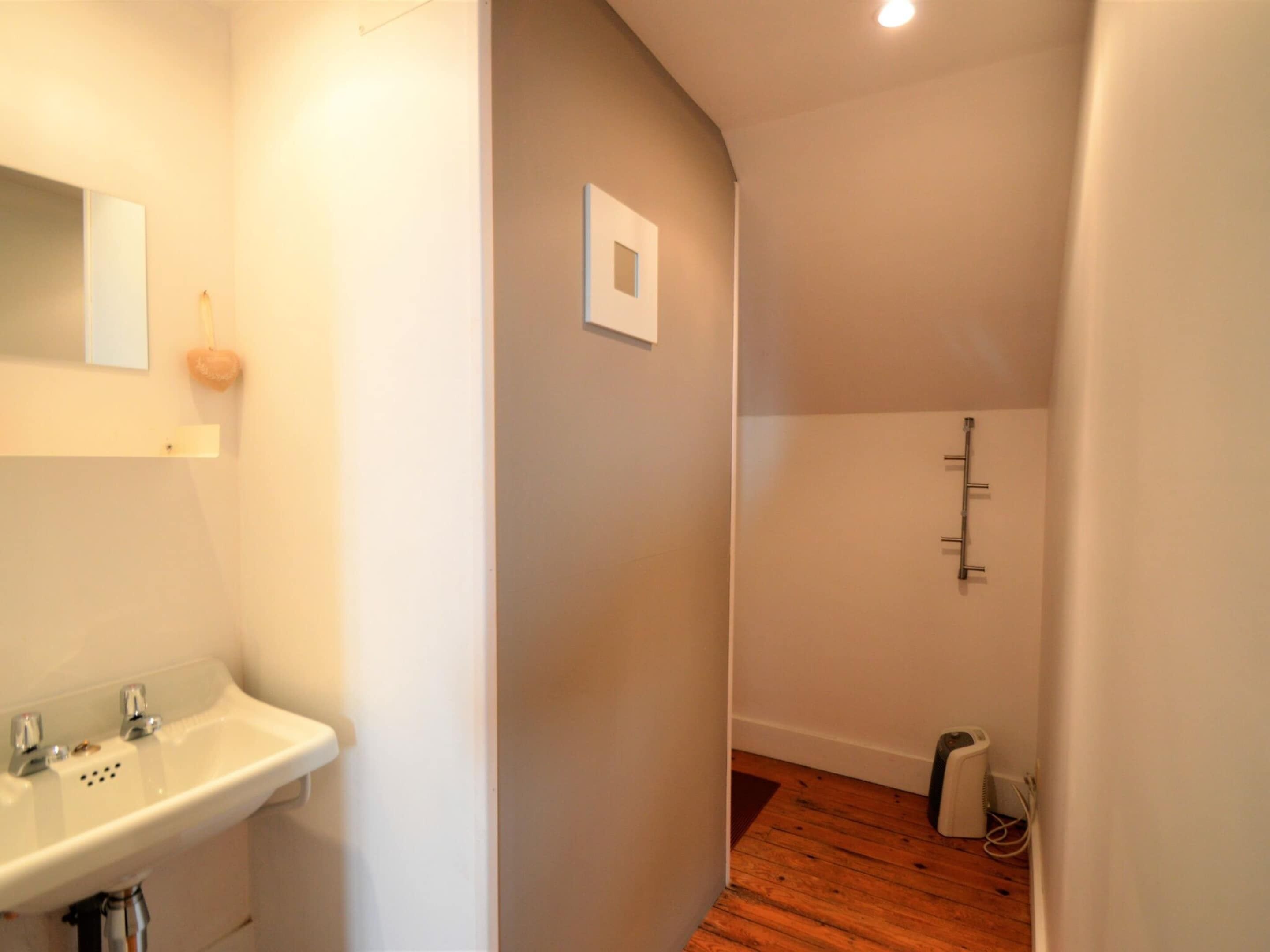 A narrow hallway with a white sink on the left, a small mirror, and a light fixture on the ceiling.