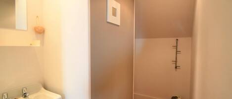 A narrow hallway with a white sink on the left, a small mirror, and a light fixture on the ceiling.