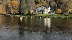 Un bâtiment blanc avec une cheminée, situé au bord d’un lac paisible, avec des arbres en arrière-plan.