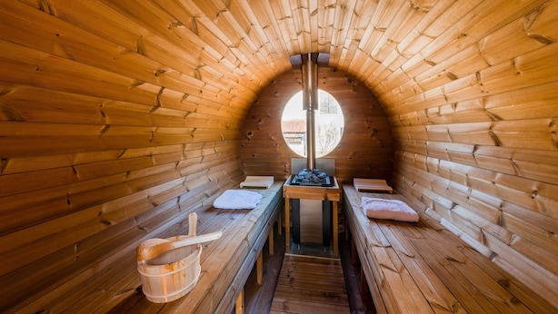 Un sauna aux murs et aux bancs en bois, avec un radiateur central et une fenêtre au fond.