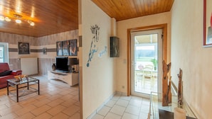 A spacious living room with a wooden ceiling, a television, a red sofa, and a dining area with chairs and a table. - Sweet Home in Chiny With Garden (Chiny)