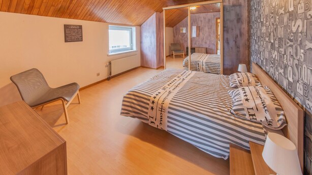A cozy bedroom with a wooden ceiling, a large mirror, a bed with patterned bedding, a chair, and a bedside table. - Sweet Home in Chiny With Garden (Chiny)