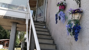 A staircase leading to a building entrance with a concrete pillar, a metal railing, and hanging flower baskets. - Sweet Home in Chiny With Garden (Chiny)