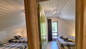 En smal hall med träväggar och dörrar som leder till två sovrum med rutigt sänglinne och kuddar.