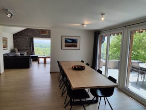 A spacious living area with a long wooden dining table, black chairs, a black sofa, and a stone accent wall. - Luxury Villa Near Durbuy (Durbuy)