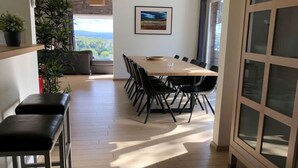 Een moderne eetruimte met een lange tafel en zwarte stoelen, een houten vloer en uitzicht op het landschap door grote ramen.