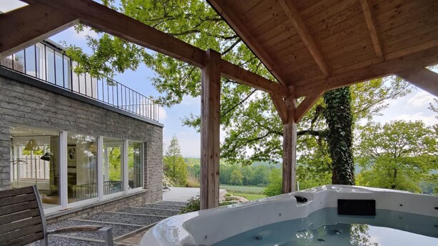 Een hottub onder een houten pergola, met uitzicht op een stenen gebouw en bomen.