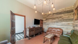 Una sala de estar con un sofá de cuero marrón, un sillón de cuero verde, un mueble de madera y un televisor montado en una pared de madera.