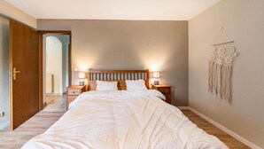Ein Schlafzimmer mit einem hölzernen Bett, zwei Nachttischen mit Lampen, einem an der Wand befestigten Traumfänger und einer Tür zu einem anderen Raum.