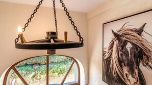 Ein Zimmer mit einem großen Fenster, einer hängenden Leuchte und einem gerahmten Bildnis eines Pferdes an der Wand.