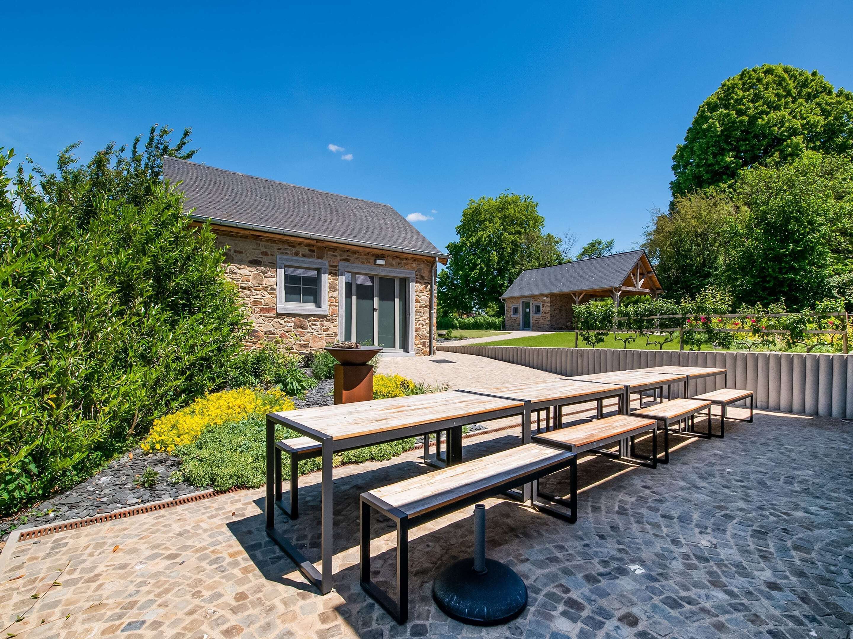 An outdoor patio with stone flooring, wooden benches, and a stone building in the background.