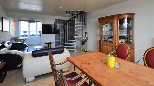 A modern living room with a dining area, a staircase, and a wooden cabinet with glass doors. - Rochehaut Hideaway With Tub (Bouillon)