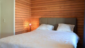 A bedroom with a wooden slat wall, a bed with white linens, and a nightstand with a lamp. - Rochehaut Hideaway With Tub (Bouillon)
