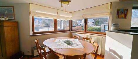 A dining area with a round wooden table, chairs, and a window with a view of buildings and trees.