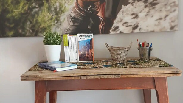 Une table en bois, sur laquelle on trouve un set de table en fibres tressées, une plante en pot, un panier et une collection de livres et de stylos.