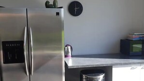 Une cuisine équipée d’un réfrigérateur en acier inoxydable, d’une bouilloire, d’une poubelle et d’une horloge murale.