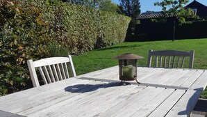 Une table en bois, surmontée d’une lanterne en métal, et entourée de chaises blanches.