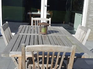 Una mesa de madera al aire libre con sillas, un farol y una puerta de cristal que da a un espacio interior.