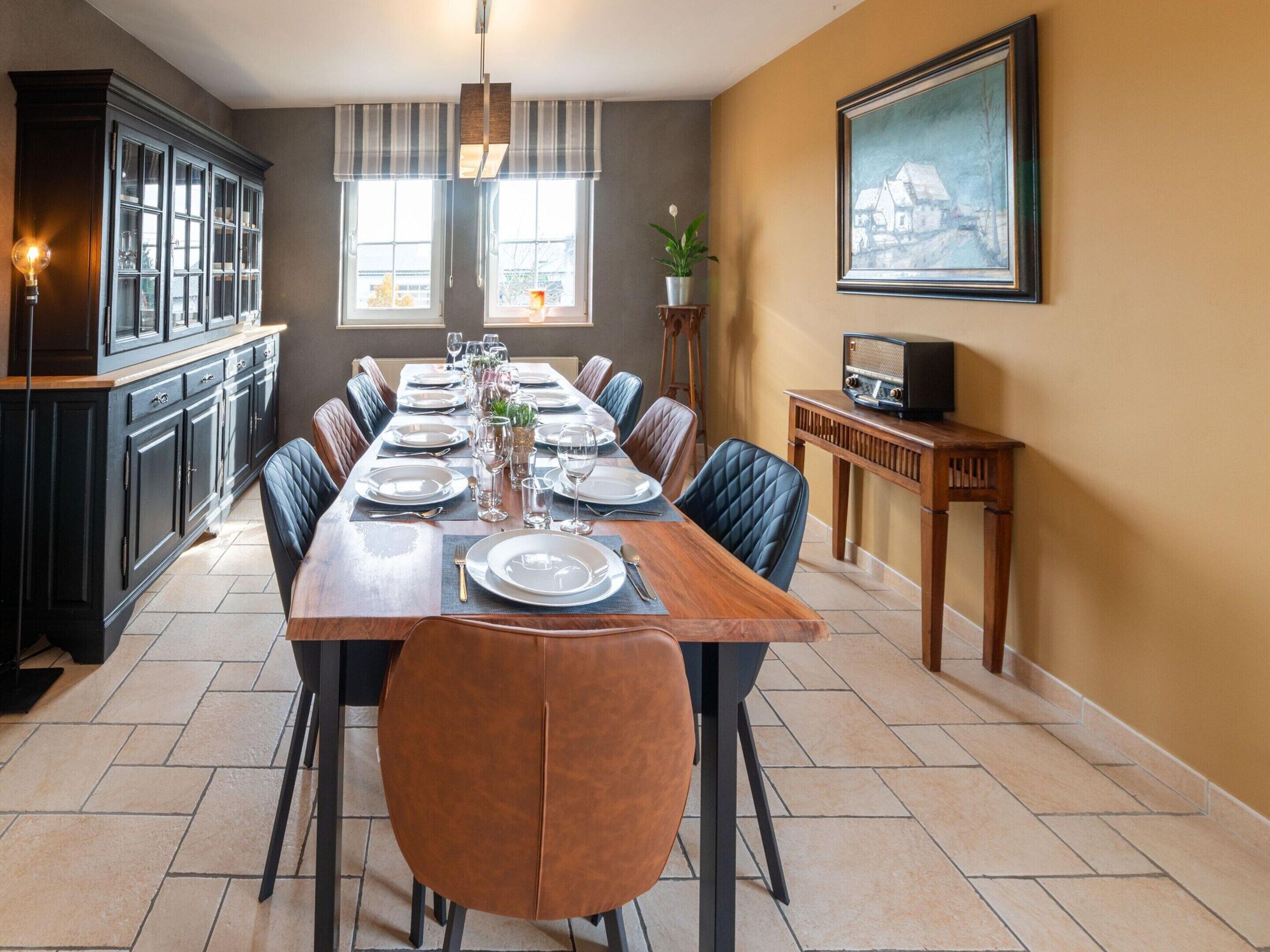 A dining room with a long table set for six, flanked by dark cabinets and a wooden sideboard.