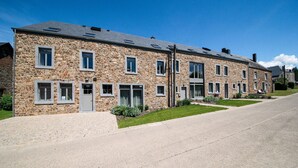 A row of stone buildings with multiple windows and doors, a paved driveway, and a clear blue sky. - Luxury Stay; La Croix Scaille (Gedinne)