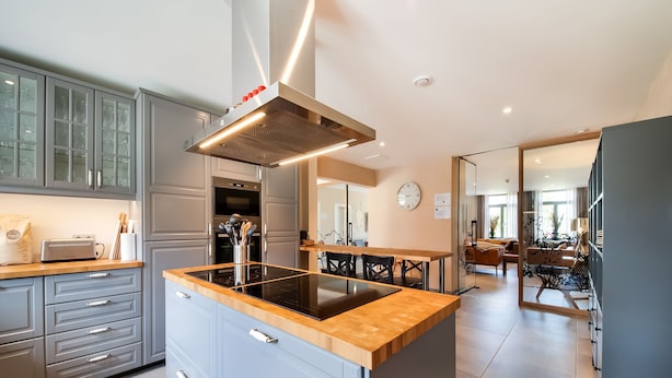 A modern kitchen with grey cabinets, a central island with a black induction cooktop, and a stainless steel range hood. - Luxury Stay; La Croix Scaille (Gedinne)