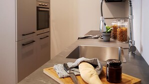 A modern kitchen with a built-in oven, stainless steel sink, and a wooden cutting board with bread and a jar of jam. - AR Boutique Apartments (Bergamo)