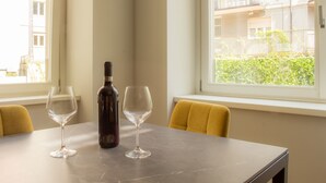 A table with two wine glasses and a bottle, a yellow chair, and a window with a view of buildings and greenery. - AR Boutique Apartments (Bergamo)
