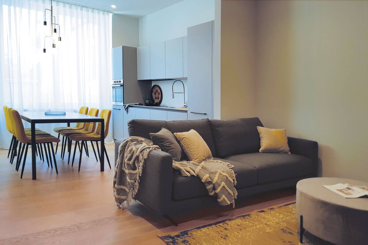 A modern living room with a sofa, a dining table with chairs, and a kitchen area in the background.