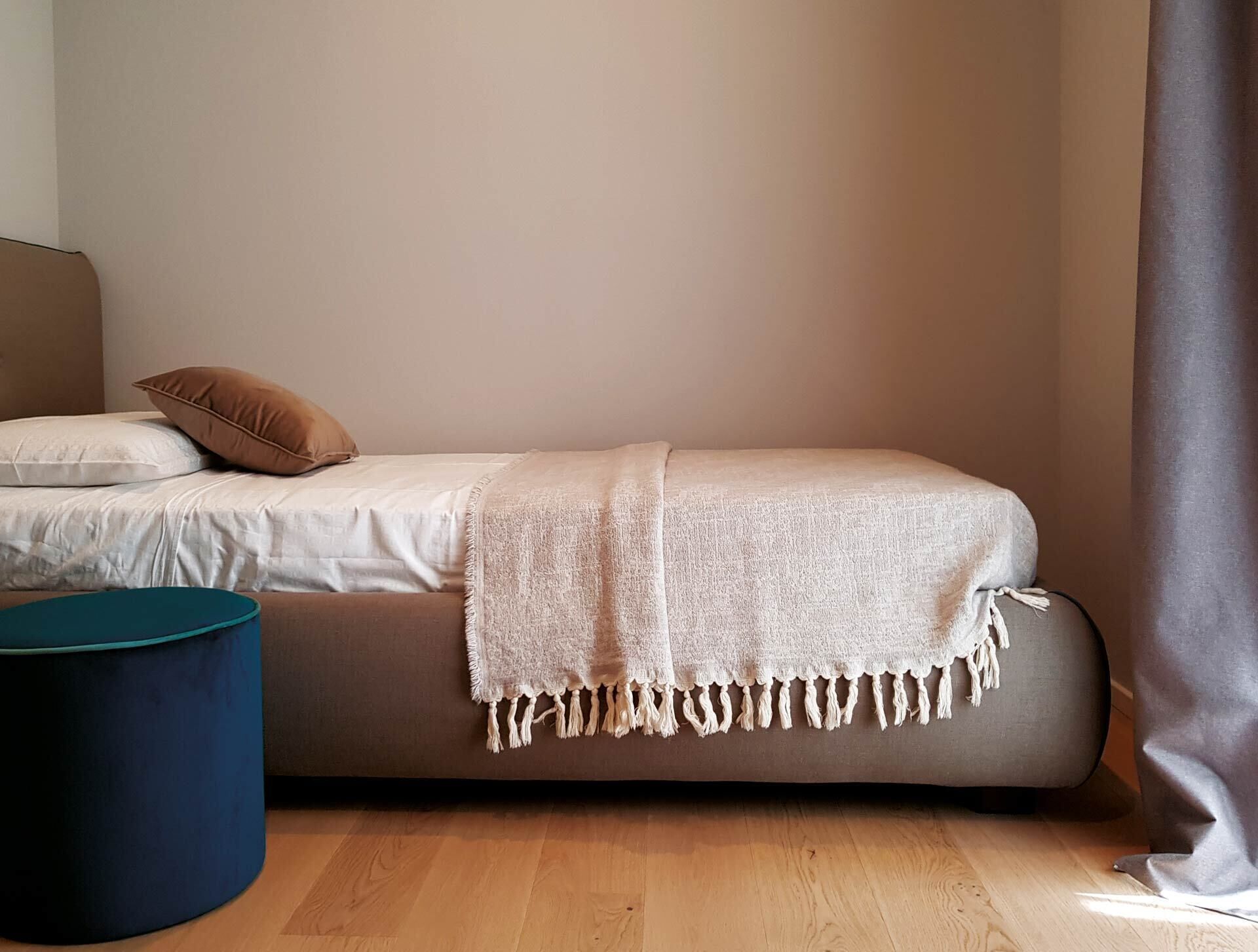 A single bed with a beige blanket, a brown pillow, and a blue ottoman.