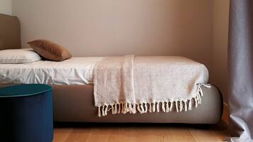 A single bed with a beige blanket, a brown pillow, and a blue ottoman.