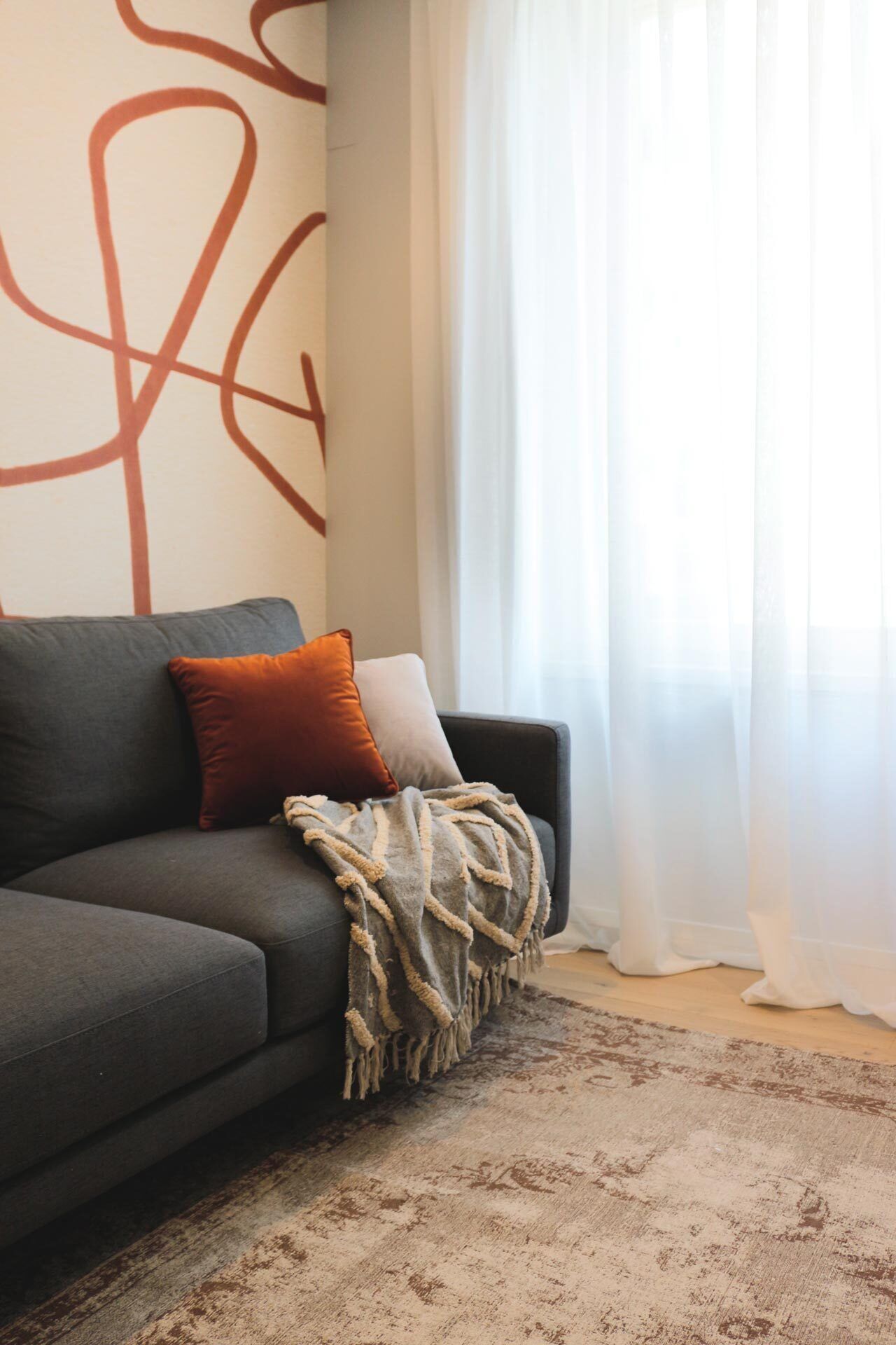 Una sala moderna con un sofá gris, una manta y dos cojines.