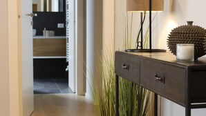 A hallway with a wooden floor, a black console table with a lamp, a potted plant, and a doorway leading to a room. - AR Boutique Apartments (Bergamo)