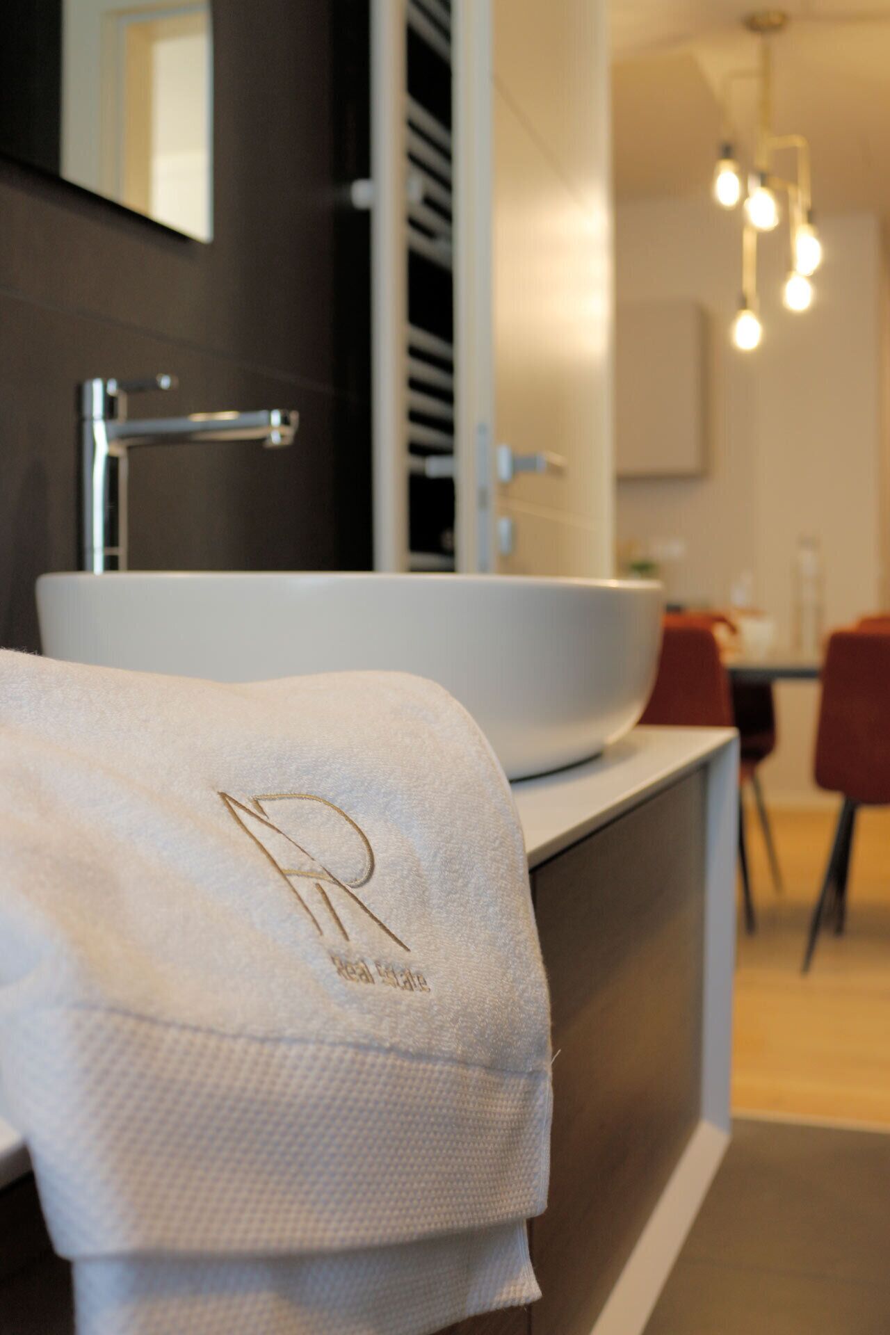 Een moderne badkamer met een groot wit wastafel, een handdoek met een monogram en een zichtbare douchehoek.