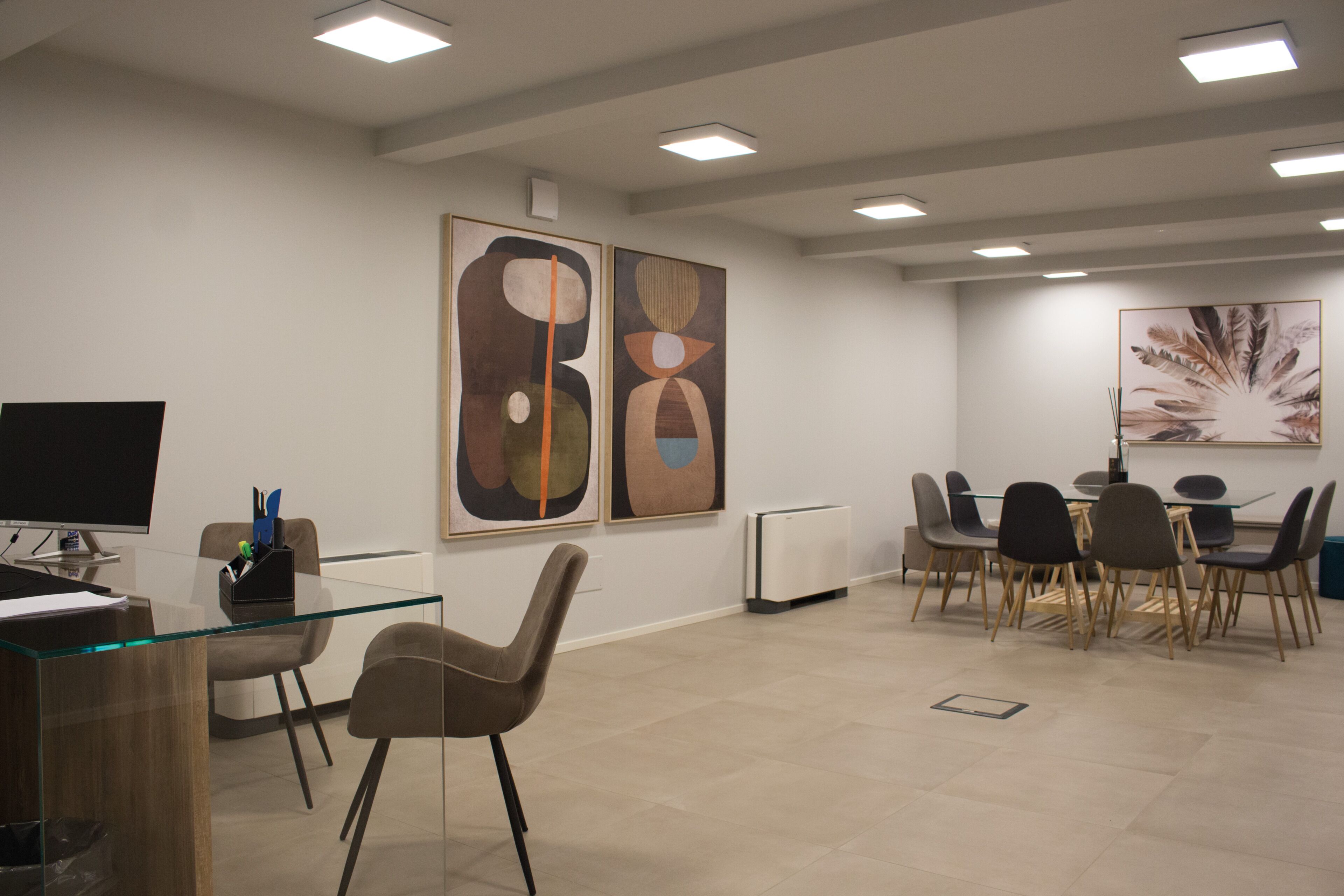 Un espace de bureau moderne avec un bureau en verre, des chaises marron, un ordinateur et des œuvres d’art abstraites accrochées aux murs.