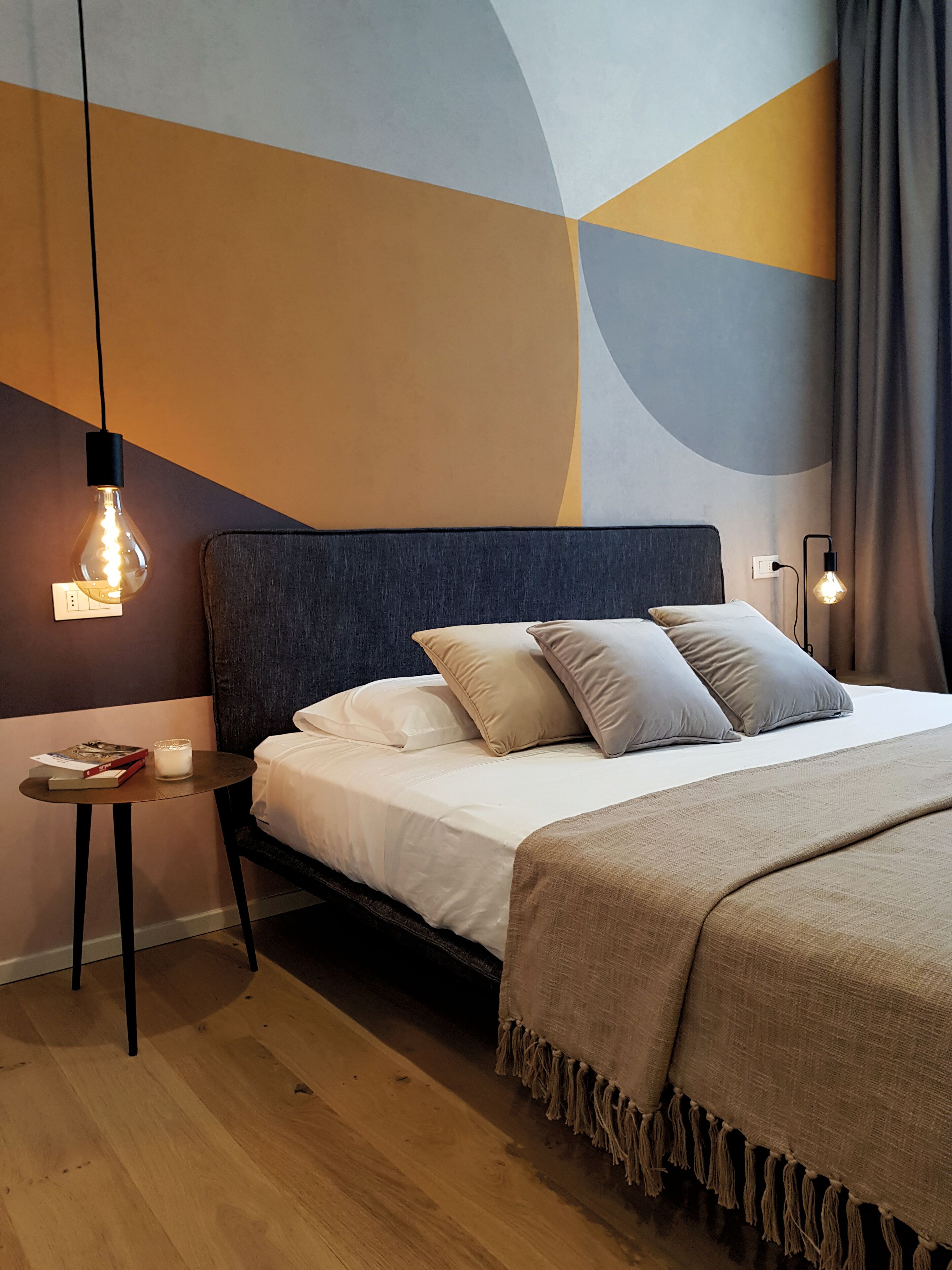 Ein modernes Schlafzimmer mit Bett, Nachttischen und einem geometrischen Wandmuster.