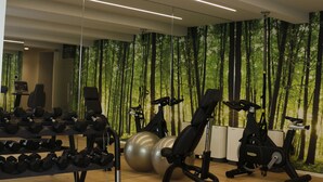 A modern gym with exercise equipment, a mirrored wall, and a forest-themed wallpaper. - AR Boutique Apartments (Bergamo)