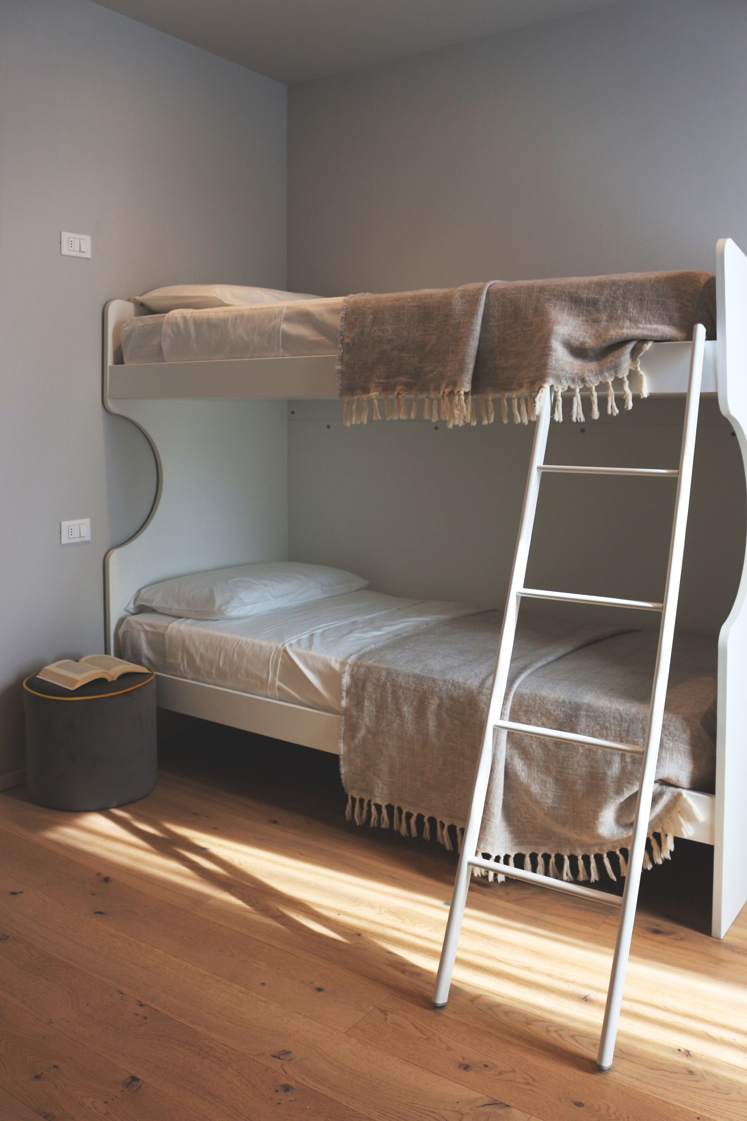 Una cama litera con una escalera, una mesita de noche pequeña y un cubo de basura.