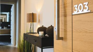 A modern interior with a wooden floor, a black console table with a lamp, and a wall-mounted number plate displaying '303'.