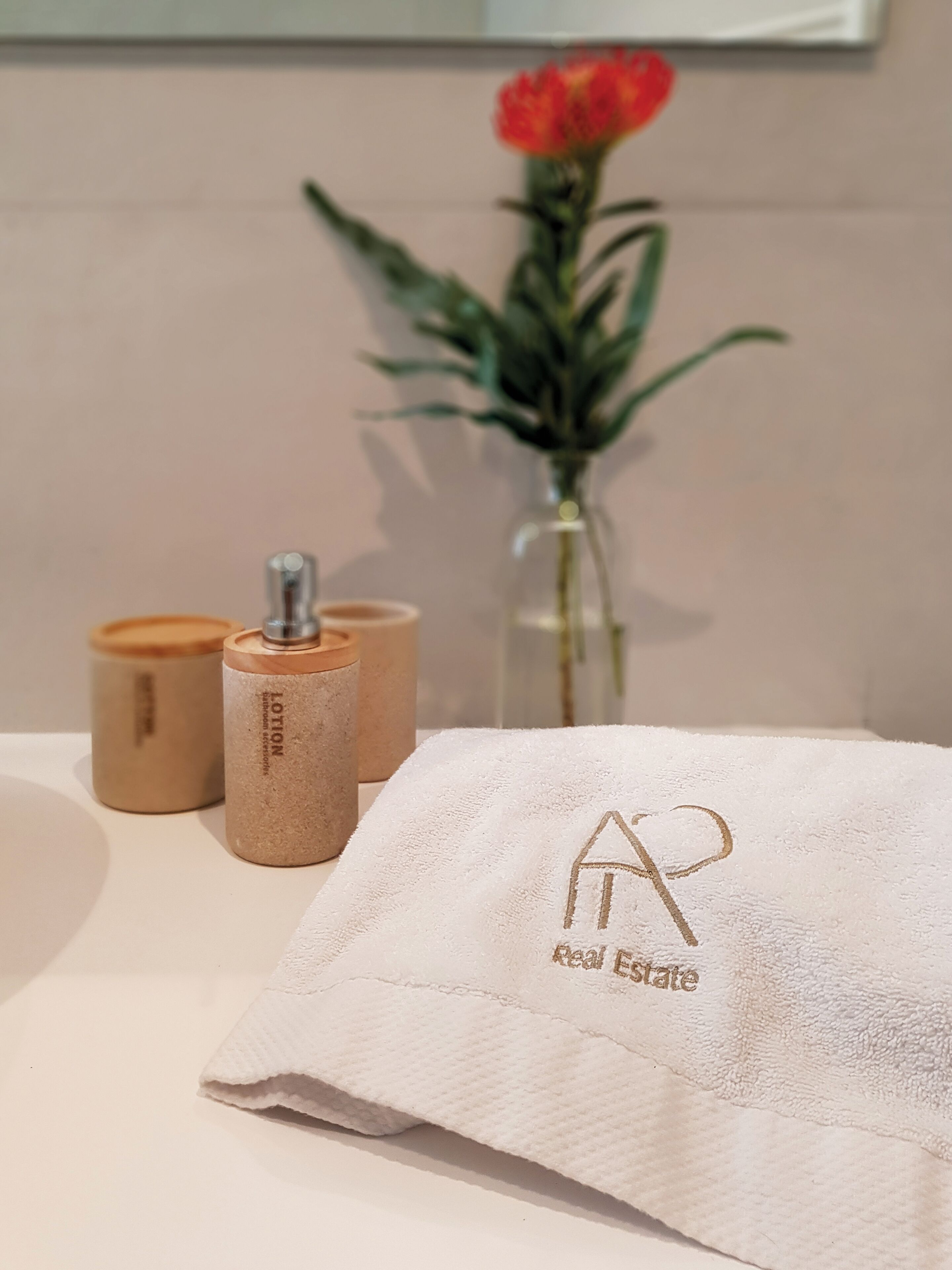 A bathroom with a towel, two lotion containers, and a vase with a flower.