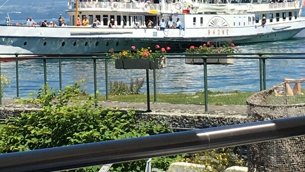 Un grand bateau à plusieurs ponts, portant le nom « RHONE » sur sa coque, était amarré à un quai, avec un ciel dégagé en arrière-plan.