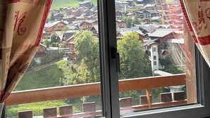 Une fenêtre donnant sur un village, des rideaux à motifs et une rambarde en bois.