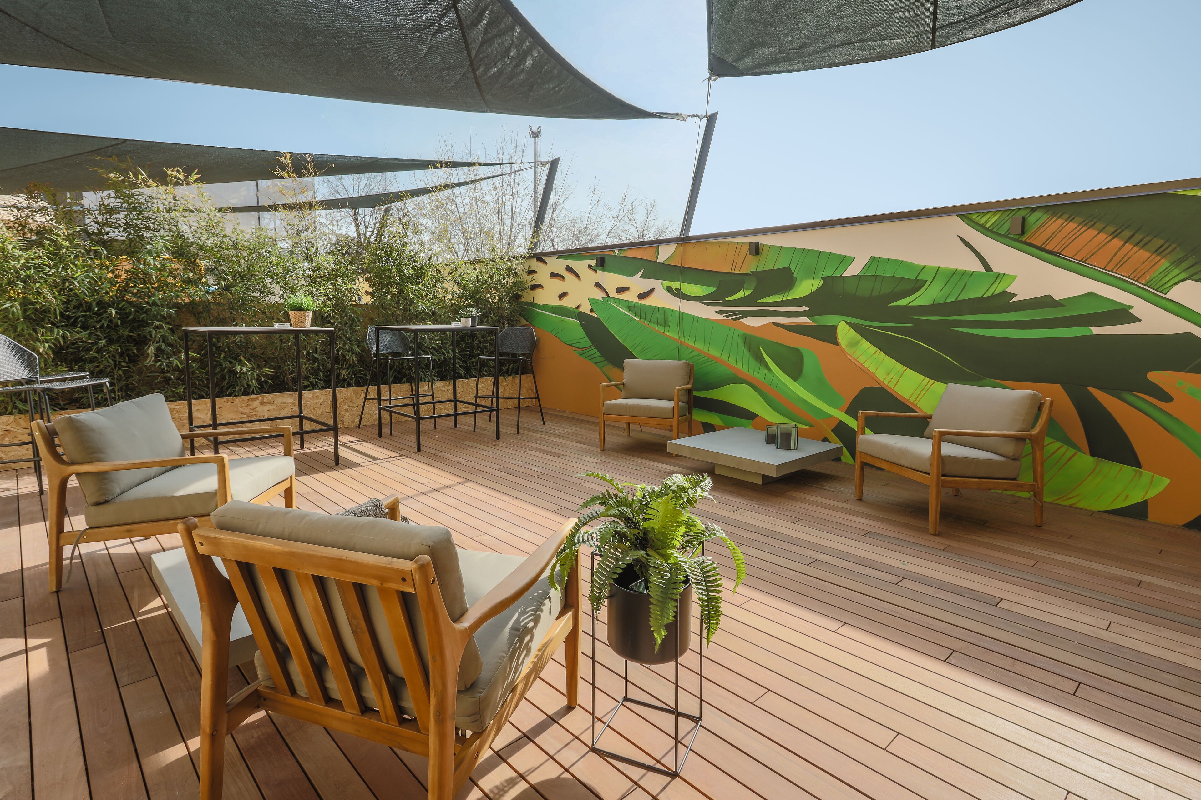 An outdoor patio with wooden flooring, several chairs, a table, and a large mural of tropical leaves.