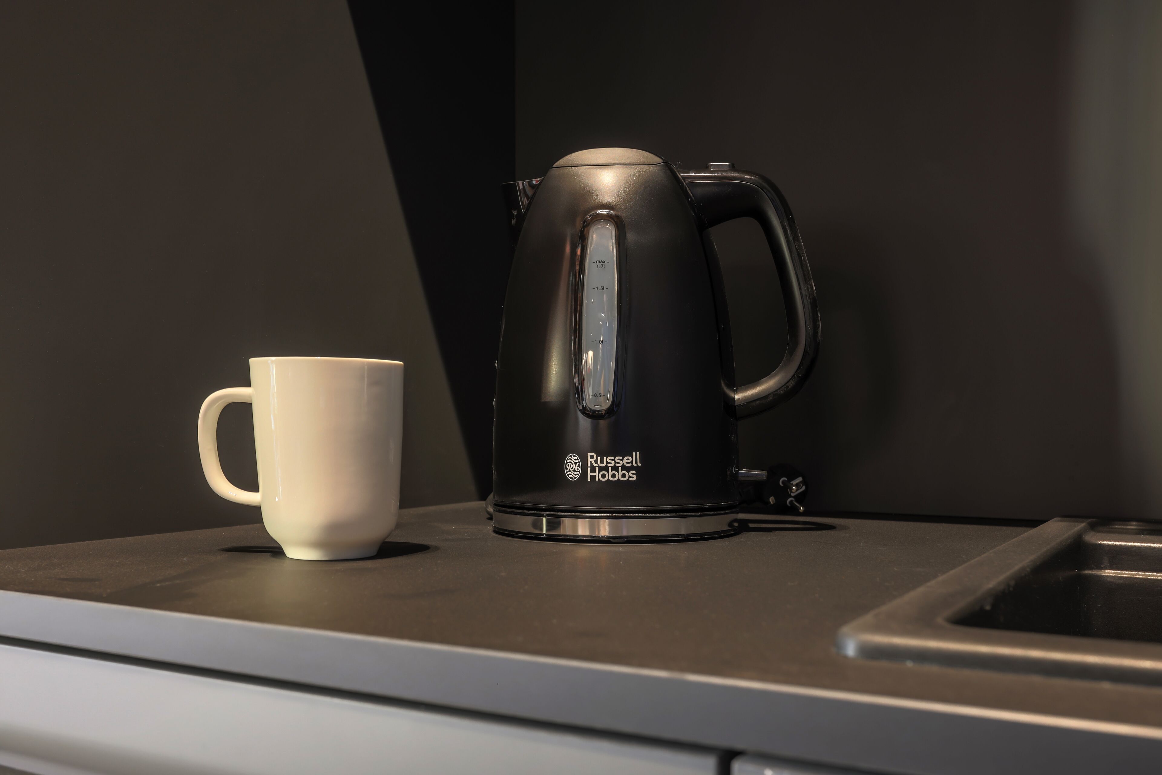 Uma chaleira elétrica Russell Hobbs preta sobre uma bancada, ao lado de uma caneca branca.