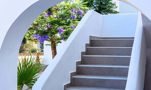 A staircase with a white wall and a tree with purple flowers. - Aelia Suites (Agios Nikolaos)