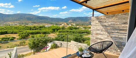 A balcony with a view of mountains, a stone wall, and two black chairs.