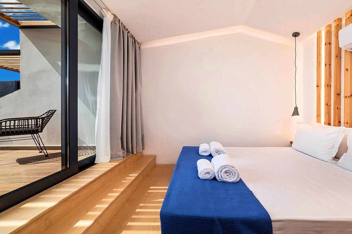 A modern hotel room with a bed, a blue towel, a chair, and a large window.